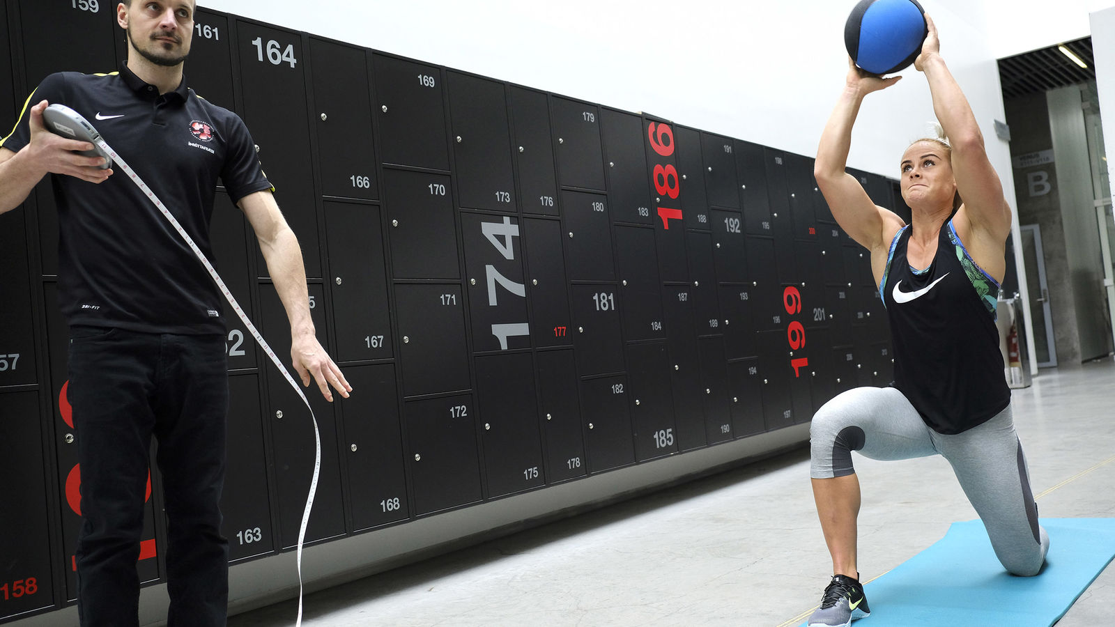 A woman prepares to throw a ball while a man measures the distance